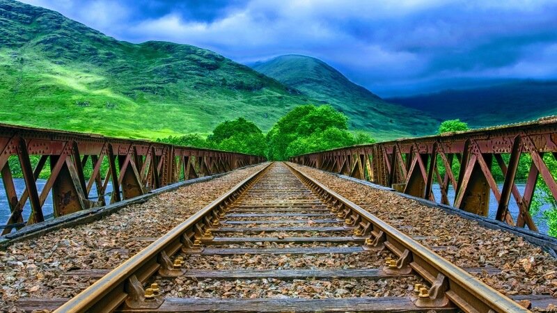 train track bridge with clouds and green hills